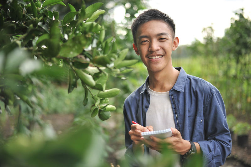 Happy of smiling young asian farmer male holding the notebook on green garden