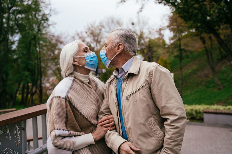 Smiling senior couple wearing mask embracing while standing outdoors