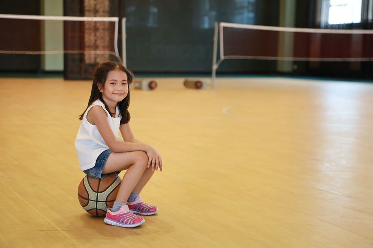 Full length portrait of girl sitting on basketball