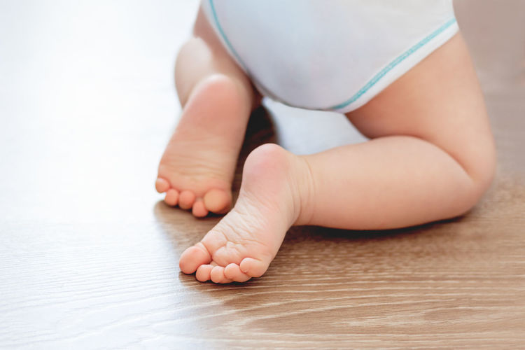 Baby's feet on wooden floor. bare heels of little child wearing white bodysuit and diaper. 