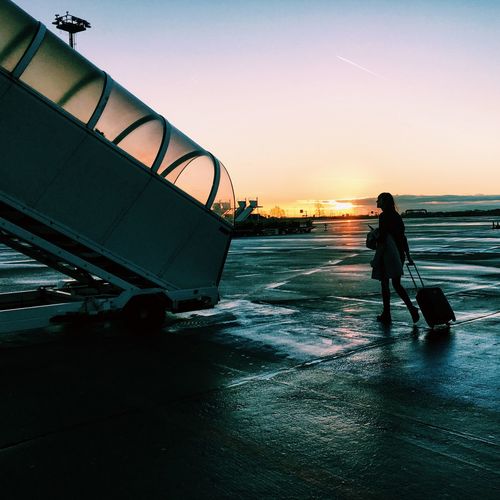 Woman walking towards staircase at airport against sky during sunset