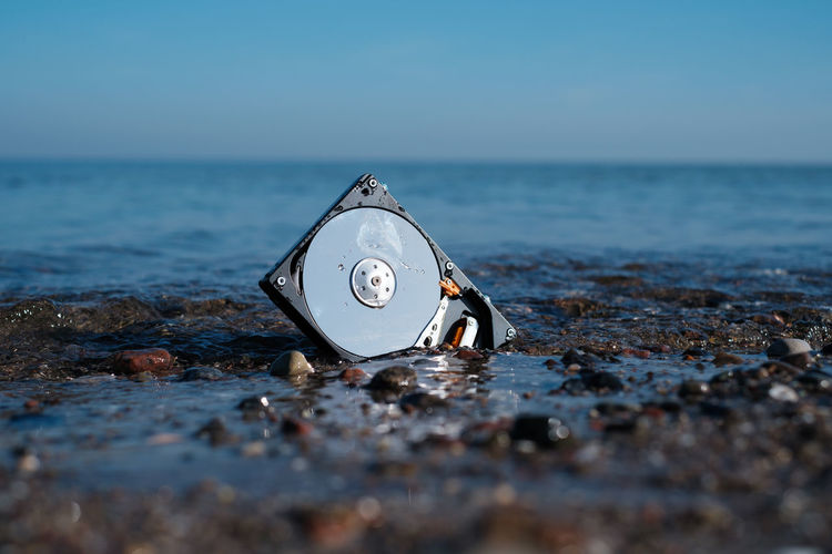 A computer hard disk lies in the shore sand of the sea and is washed by the water