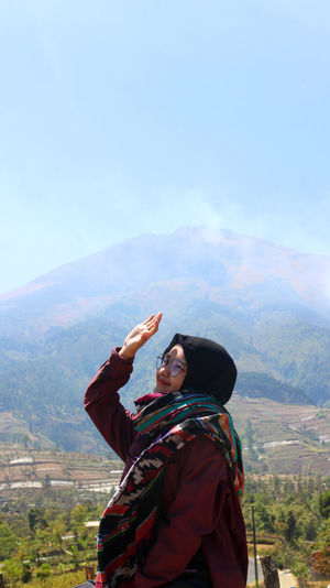 Woman shielding eyes while standing on mountain against sky