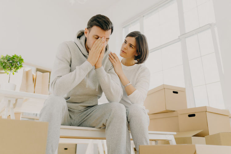 Woman consoling tired man sitting by boxes at home
