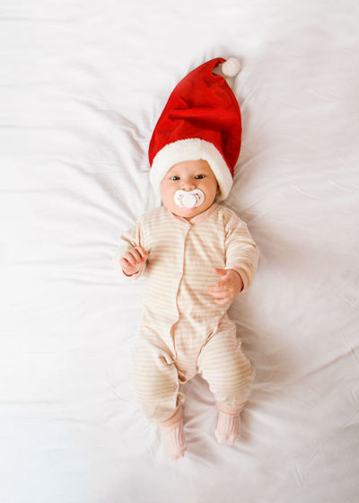 Baby in a santa hat and with a pacifier lies on the bed