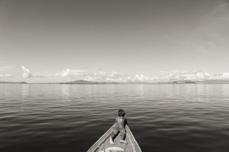 Rear view of boy lying on boat in sea against sky