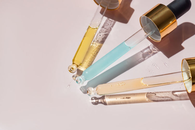 Transparent pipettes with blue and yellow cosmetics serum on a light pink background. product 