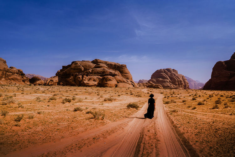 Rear view of woman walking on dirt road against sky
