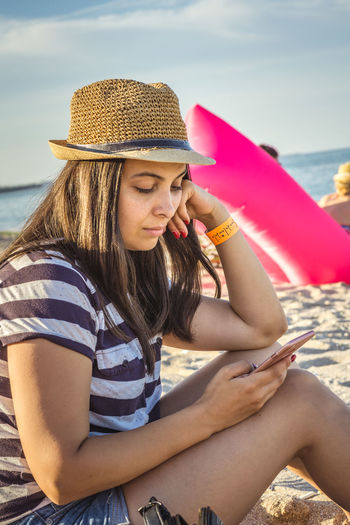 Beautiful young woman using mobile phone while sitting on beach