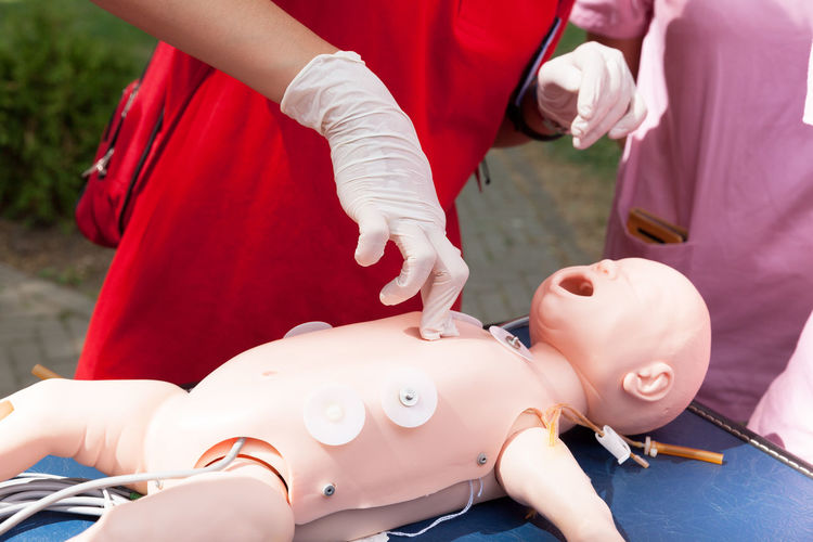 Midsection of rescue worker performing cpr on baby mannequin