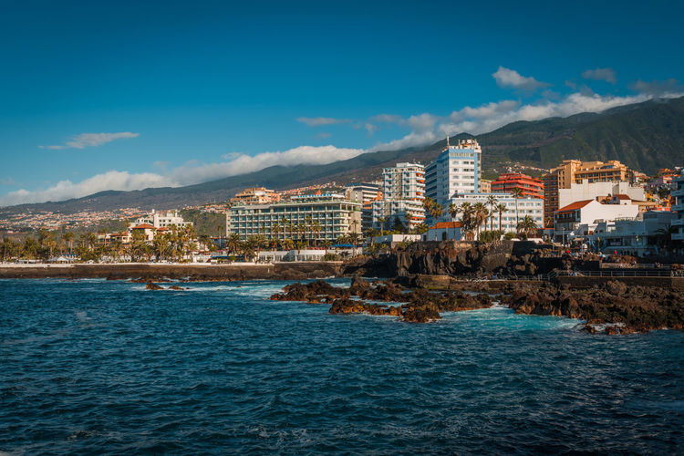 Sea by buildings in city against sky