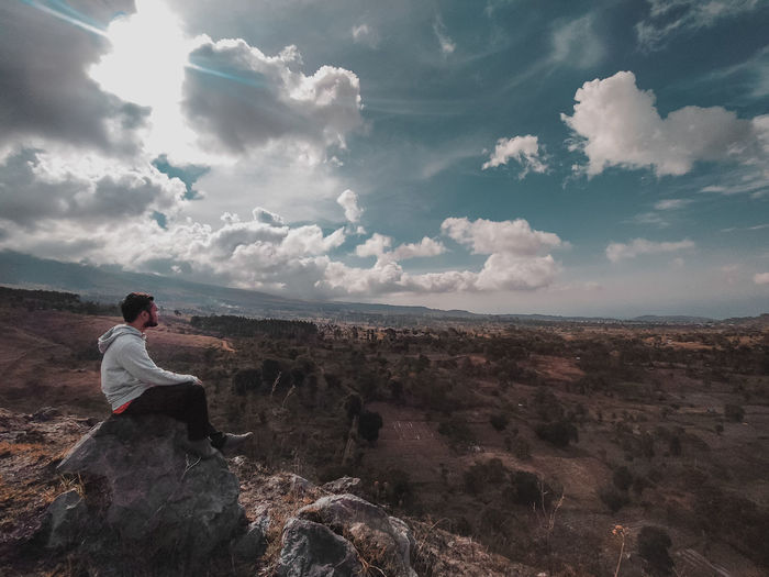 Side view of man sitting on landscape against sky