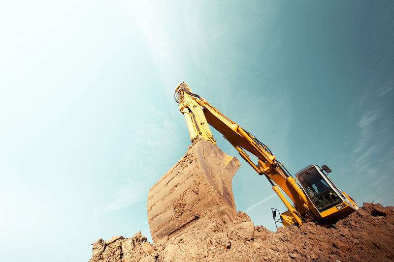 Low angle view of crane pulling mud at construction site against sky