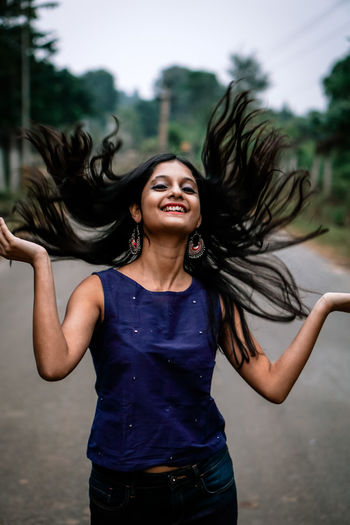 Smiling young woman tossing hair while standing on road