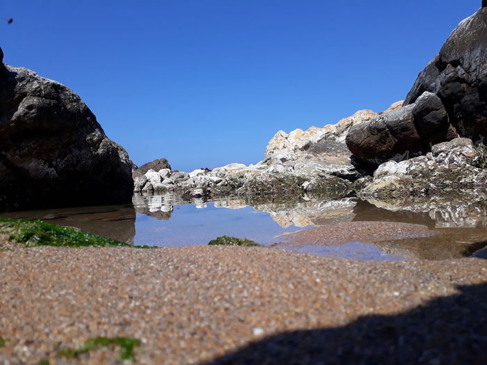 Surface level of rocks by sea against clear blue sky