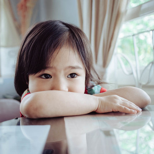 Close-up of cute girl leaning on glass table at home