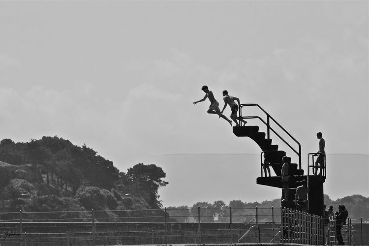 Men diving from platform against sky