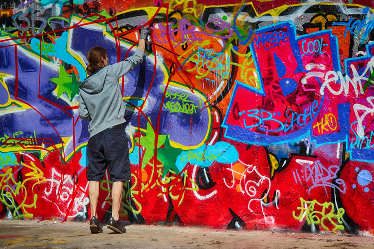 Man standing by multi colored graffiti on wall