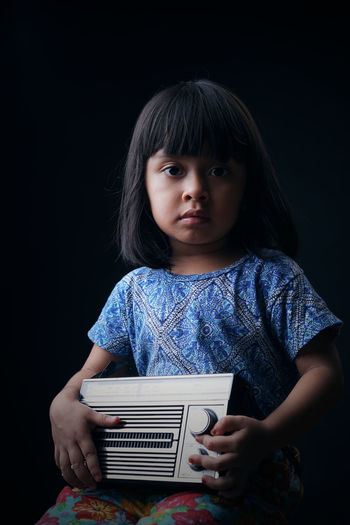 Portrait of cute girl holding radio against black background