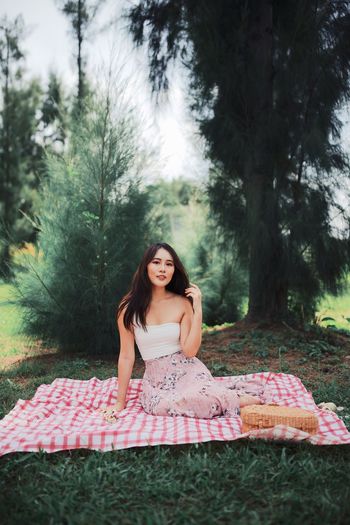 Beautiful young woman sitting on picnic blanket against trees in forest