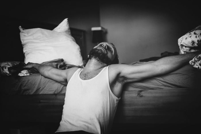 Man relaxing with arms outstretched by bed at home