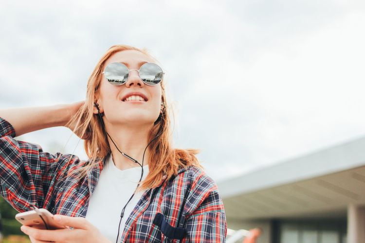 Young woman wearing sunglasses while listening to music in city