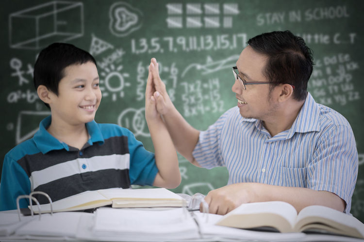 Boy with teacher at table against blackboard