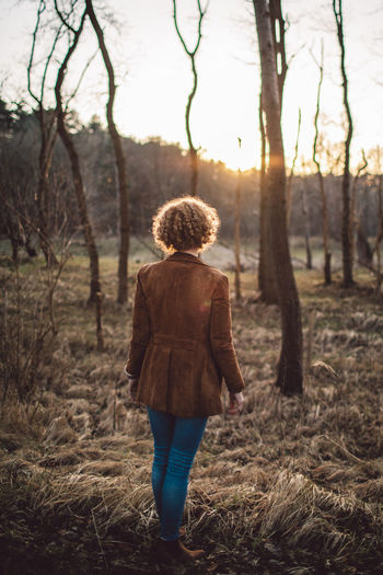 Rear view of woman walking in forest at sunset