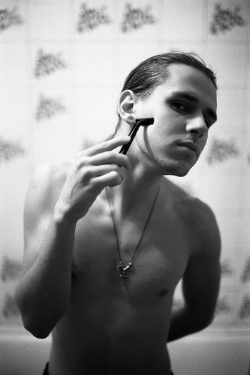 Portrait of shirtless young man shaving in bathroom at home