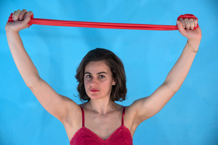 Portrait of woman holding red resistance band against blue wall