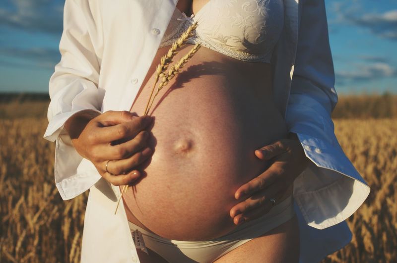 Midsection of pregnant woman standing on wheat field