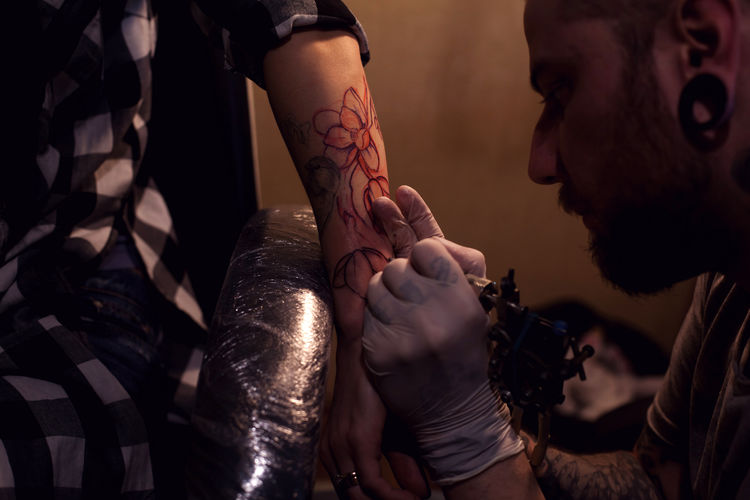 Close-up of artist tattooing woman in studio