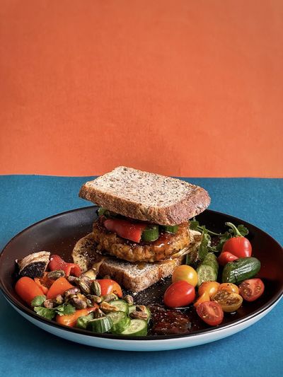 Close-up of veggie burger sandwich and fresh salad on black plate on colored background.