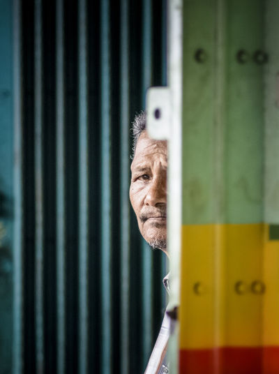 Portrait of senior man peeking through doorway