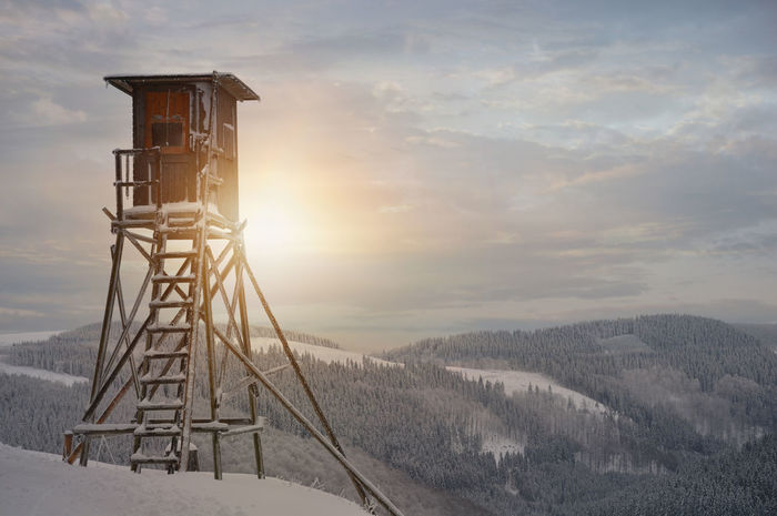 Lookout tower at snowcapped mountain against sky during sunrise