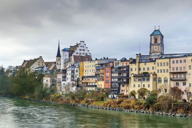 View of buildings by river against cloudy sky