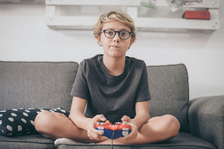 Portrait of boy playing video game while sitting on sofa in living room at home
