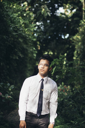 Portrait of young man standing on footpath amidst trees in park