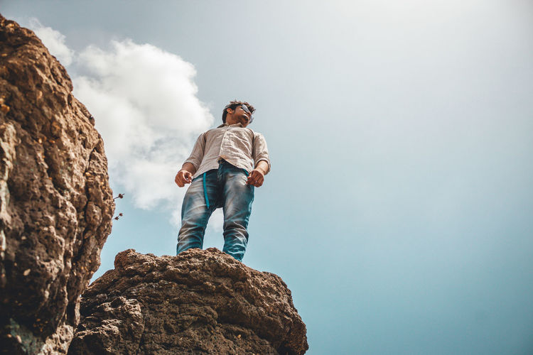 Low angle view of man standing on rock against sky
