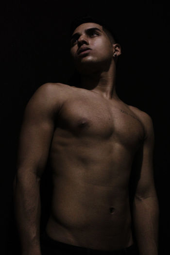 Shirtless young man looking away against black background