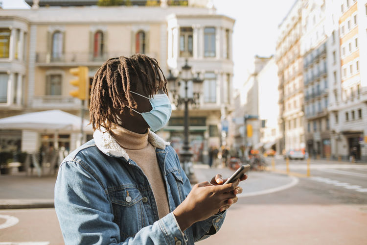 Young man with smart phone standing in city during coronavirus
