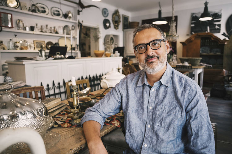 Portrait of smiling owner sitting at table in antique store