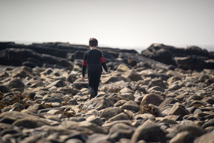 Rear view of boy walking along a rocky shore.
