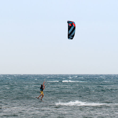 Man paragliding in sea against clear sky
