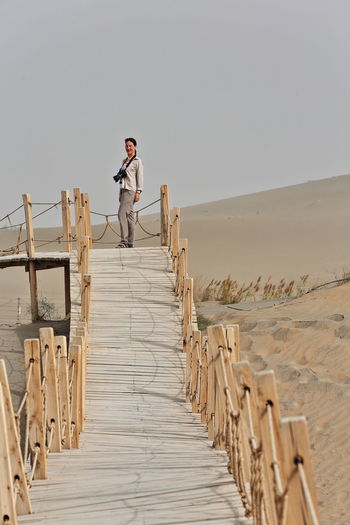 Smiling woman standing on footbridge at desert against clear sky