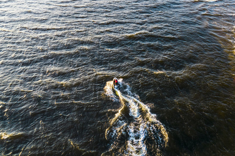 Aerial view of man rides on fast water scooter jumping on waves and making golden splashes on sunset 