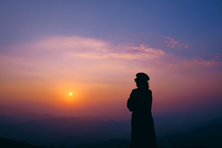 Silhouette women standing against orange sky on mountain.