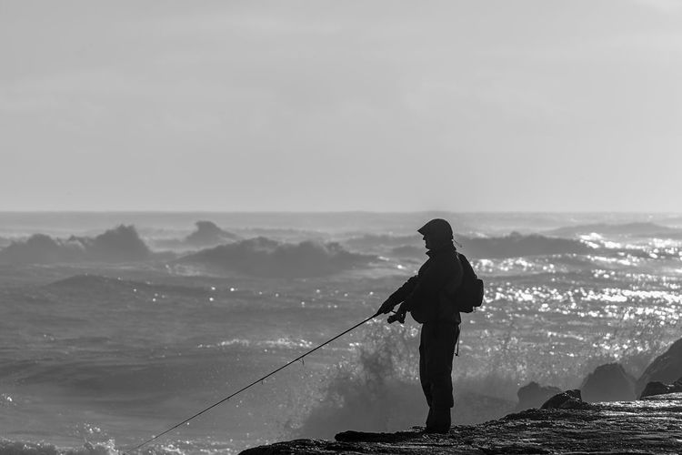 Man standing on sea fishing against sky