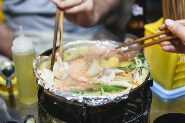Cropped image of hands holding seafood with chopsticks