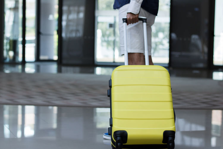 Low section of man with yellow suitcase standing in lobby at hotel
